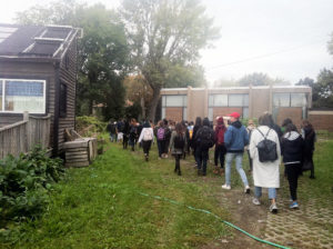 a line of twenty or so students walks across a soggy field and some outbuildings behind Concordia
